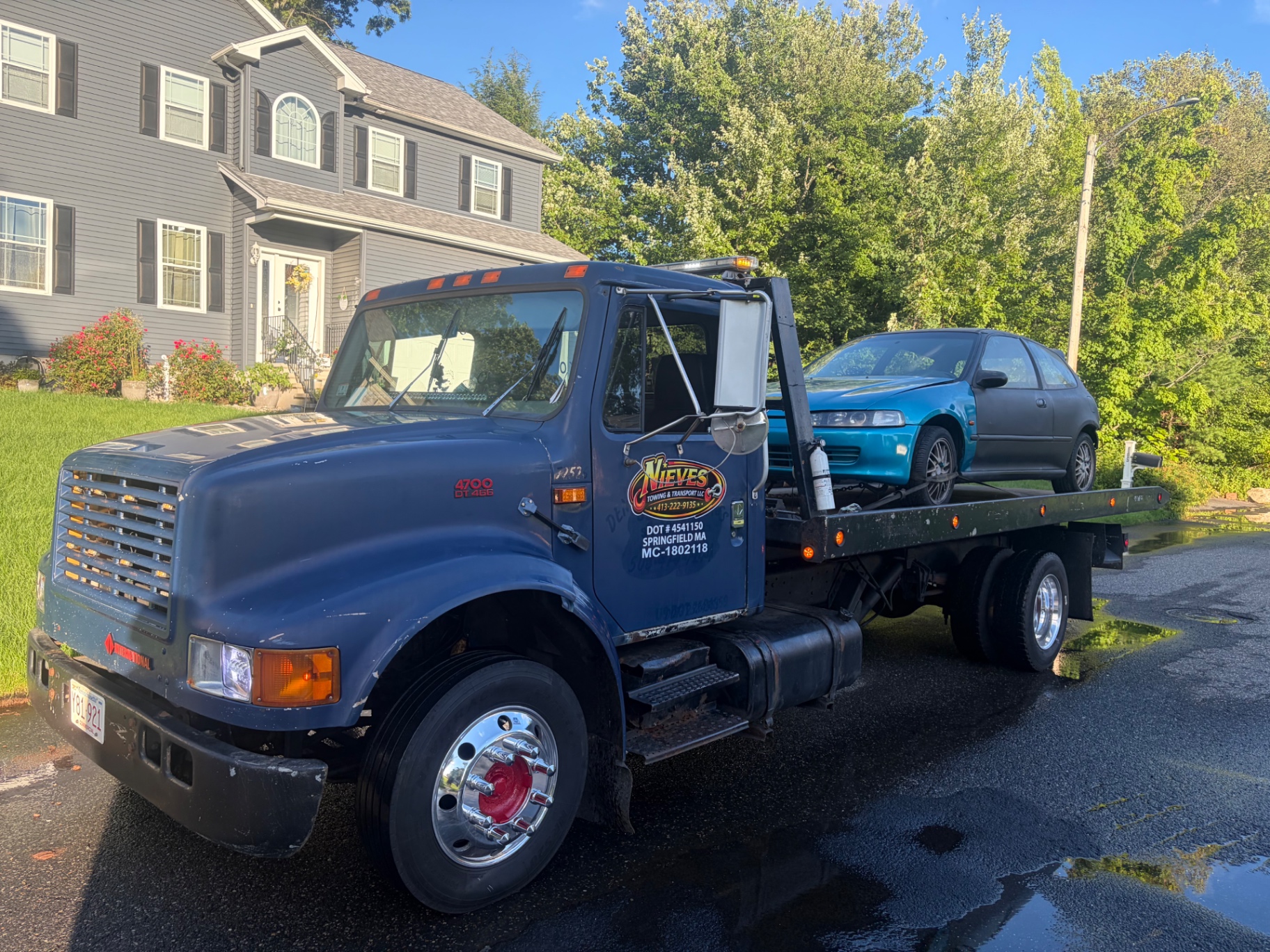 Nieves Towing flatbed with a blue hatchback loaded in a Springfield driveway