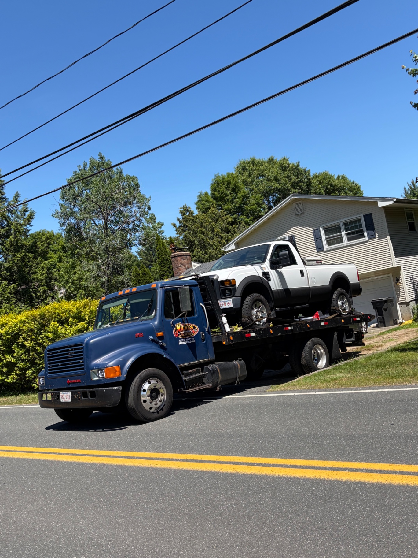 Nieves Towing rollback loading a white Ford pickup truck on a residential street